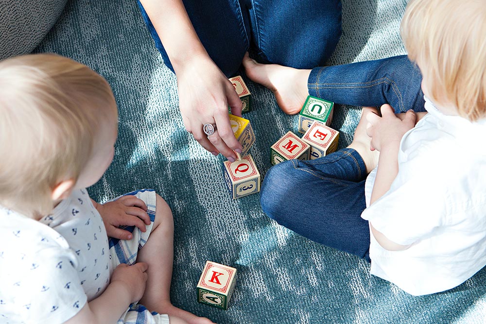 A nanny playing blocks with two small children who needed care due to a business event that was unexpected.